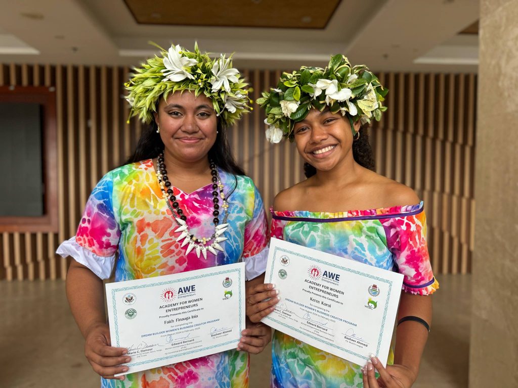 Two women in floral head dresses hold certificates