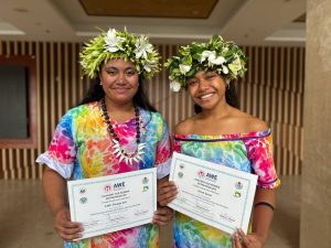 Two women in floral head dresses hold certificates