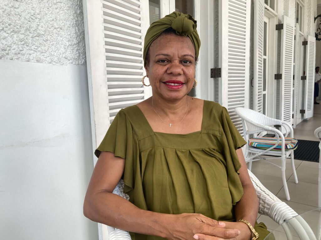 Woman wearing green dress sits with white shutters in the background