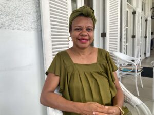 Woman wearing green dress sits with white shutters in the background